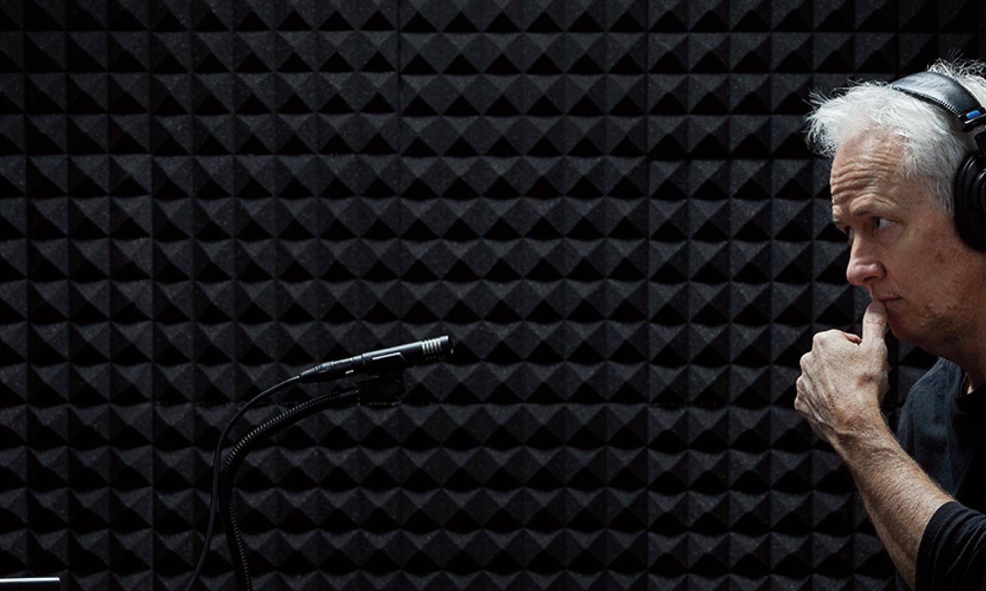 John Biewin standing in a recording booth in front of a microphone with headphones